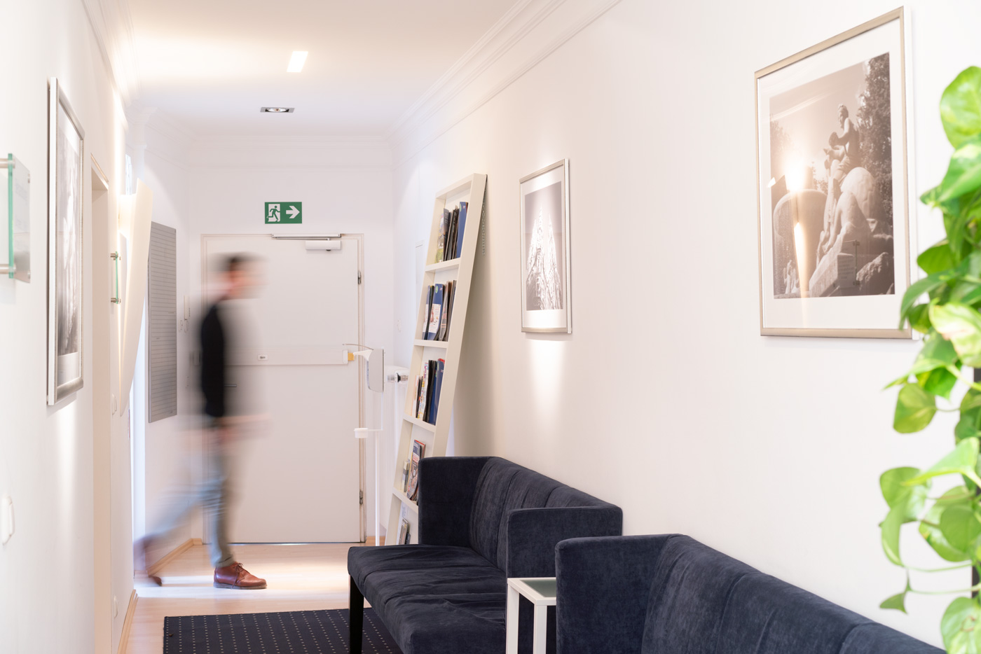 Flur und Warteraum der Praxis mit Sofas, Person läuft durch das Bild