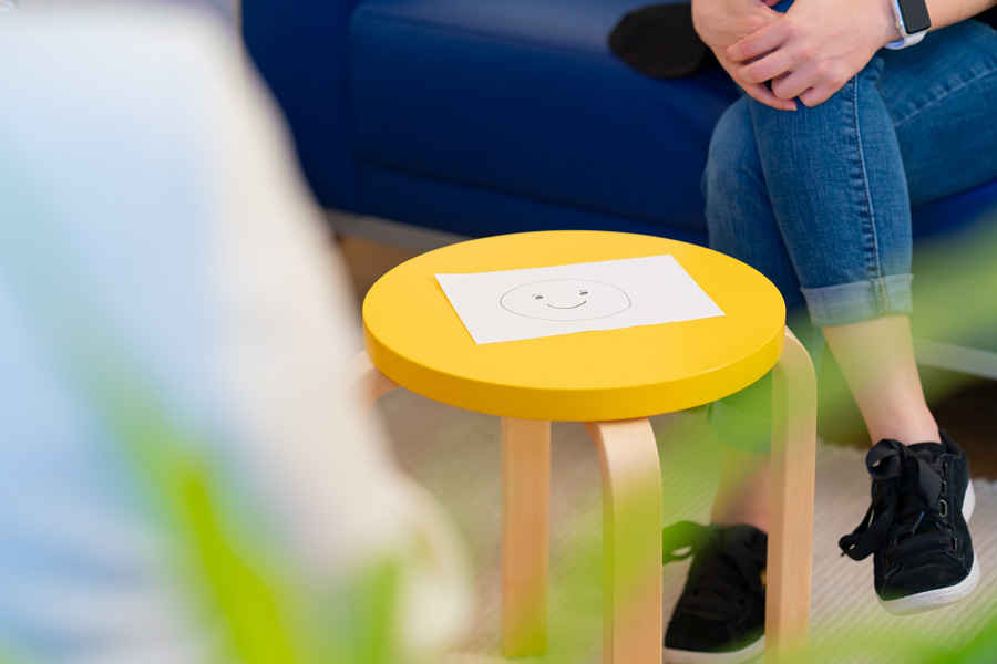 Blatt Papier mit einem lächelnden Smiley auf einem gelben Tisch, Visualisierung für emotionsfokussierte Therapie